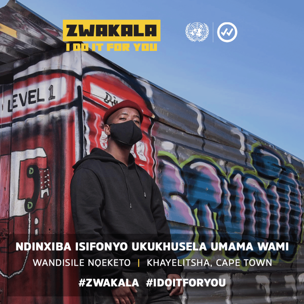 A young man leaning against a graffiti mural wears a black mask. The top reads Zwakala, I do it for you. Below reads “NDINXIBA ISIFONYO UKUKHUSELA UMAMA WAMI WANDISILE NOKETO KHAYLITSHA, CAPE TOWN”